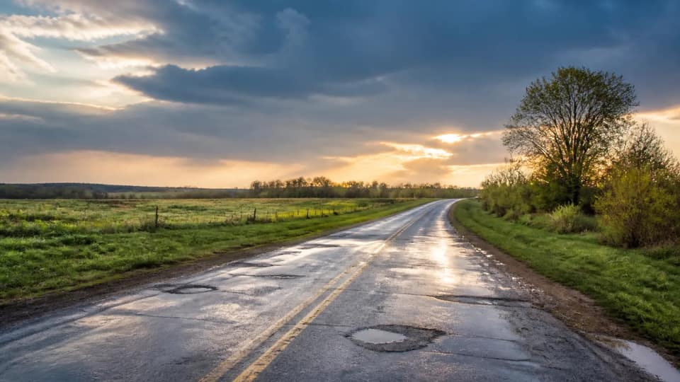 A rain-slick two-lane road through green spring farmland